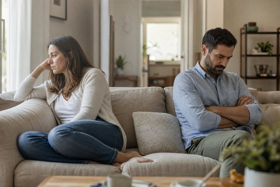 Couple sitting apart on a sofa after an argument, both looking away