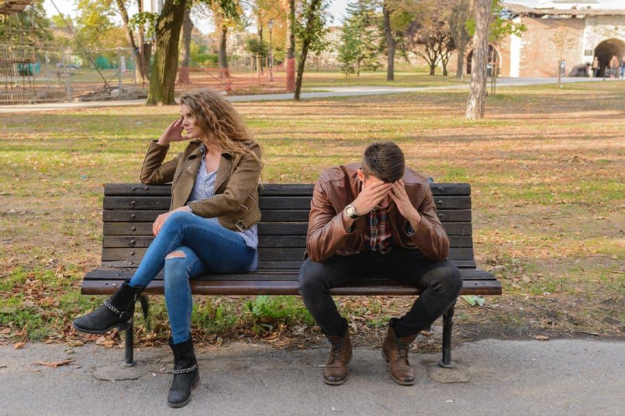 A tense couple sitting apart on a park bench