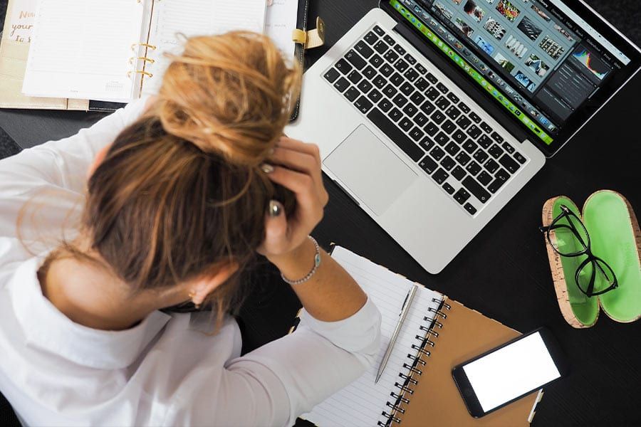 A woman with her head in her hands at a desk with a laptop