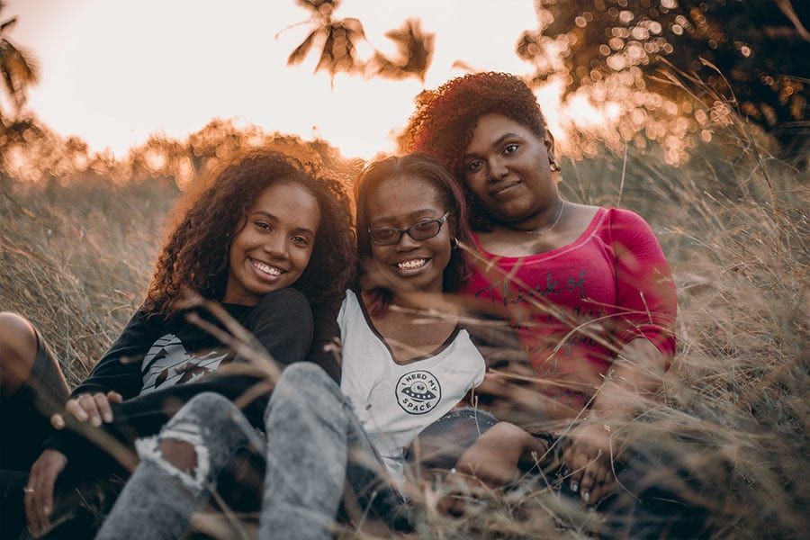 Three women smiling together outdoors at sunset